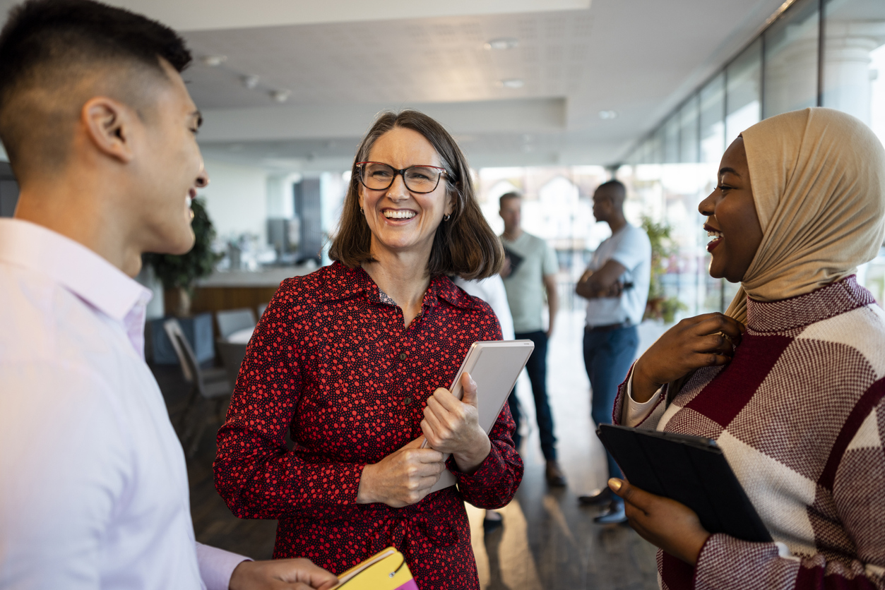 inclusive group of asian man, white woman and african woman with head wrap speak in a business hallway