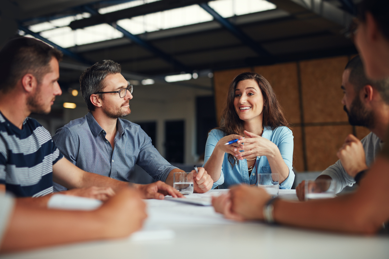 two men listen as a woman shares a story in a design meeting