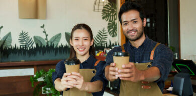 two asian baristas male and female hold out coffee cups serving gestures