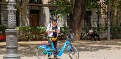 Young woman with a BiciMAD electric rental bike looking at her mobile app in a street in Madrid